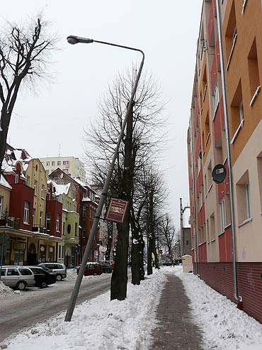 Przechylona lampa lada moment może runąć na chodnik